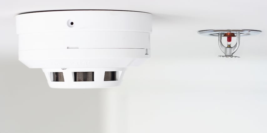 A smoke alarm and fire sprinkler head mounted to a ceiling