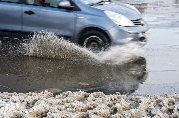 A car driving through a puddle surrounded by melting snow