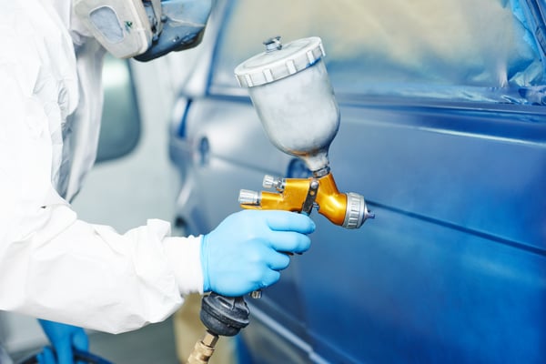 autobody employee applies paint to a car