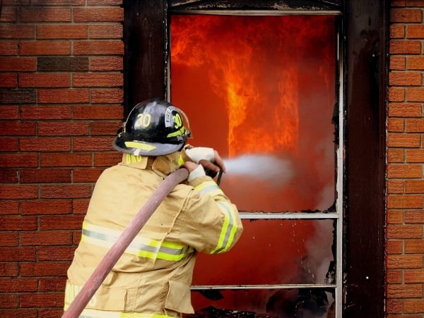 A firefighter spraying water through a doorway at flames