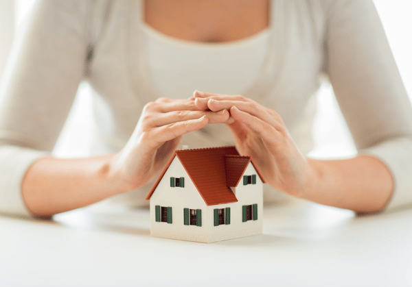 Womans hands hovering over a model home, protecting it