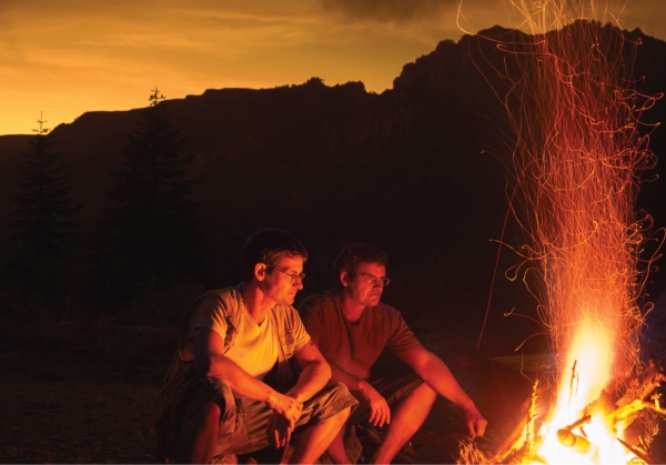 Two men sitting next to a campfire