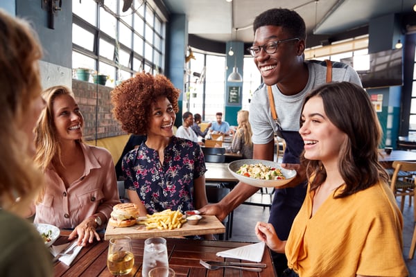 Server happily brings food to a table of smiling women